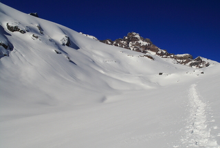 snowshoe tracks on pristine snowfield below a rocky outcrop with bright blue sky