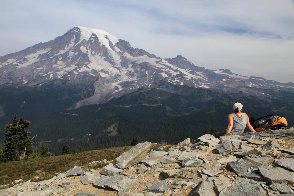 female hiker sitting on talus and looking at glaciers on Mount Rainier from Plummer Peak