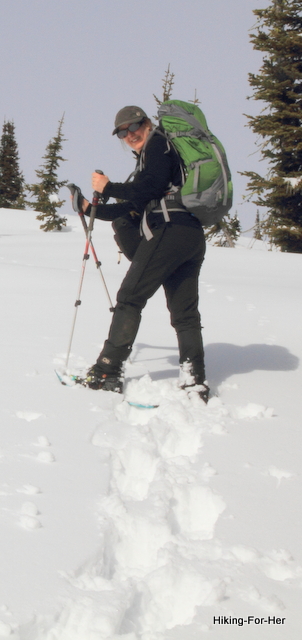 Female snowshoer with green backpack wearing sunglasses