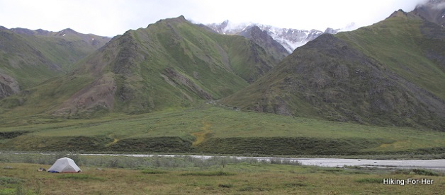 White backpacking tent in foreground, with a river and mountains in the distance on the Canning River, Alaska