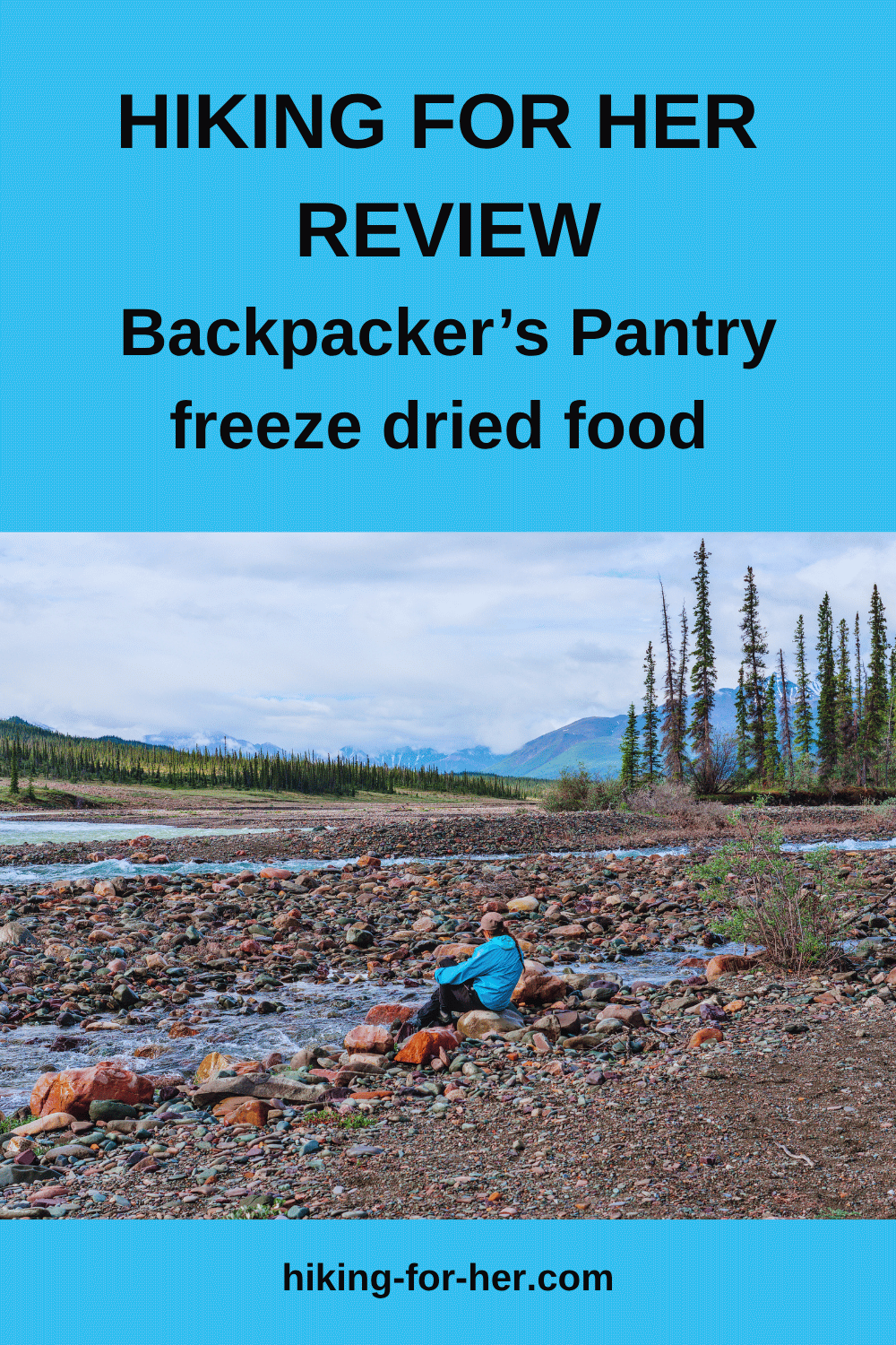 Female hiker sitting on rocky shore of creek with mountains in distance