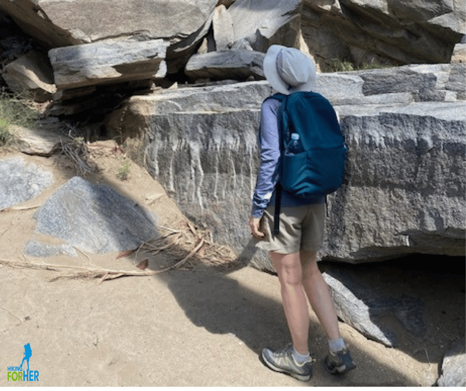 Female hiker with backpack staring up at huge rock formation