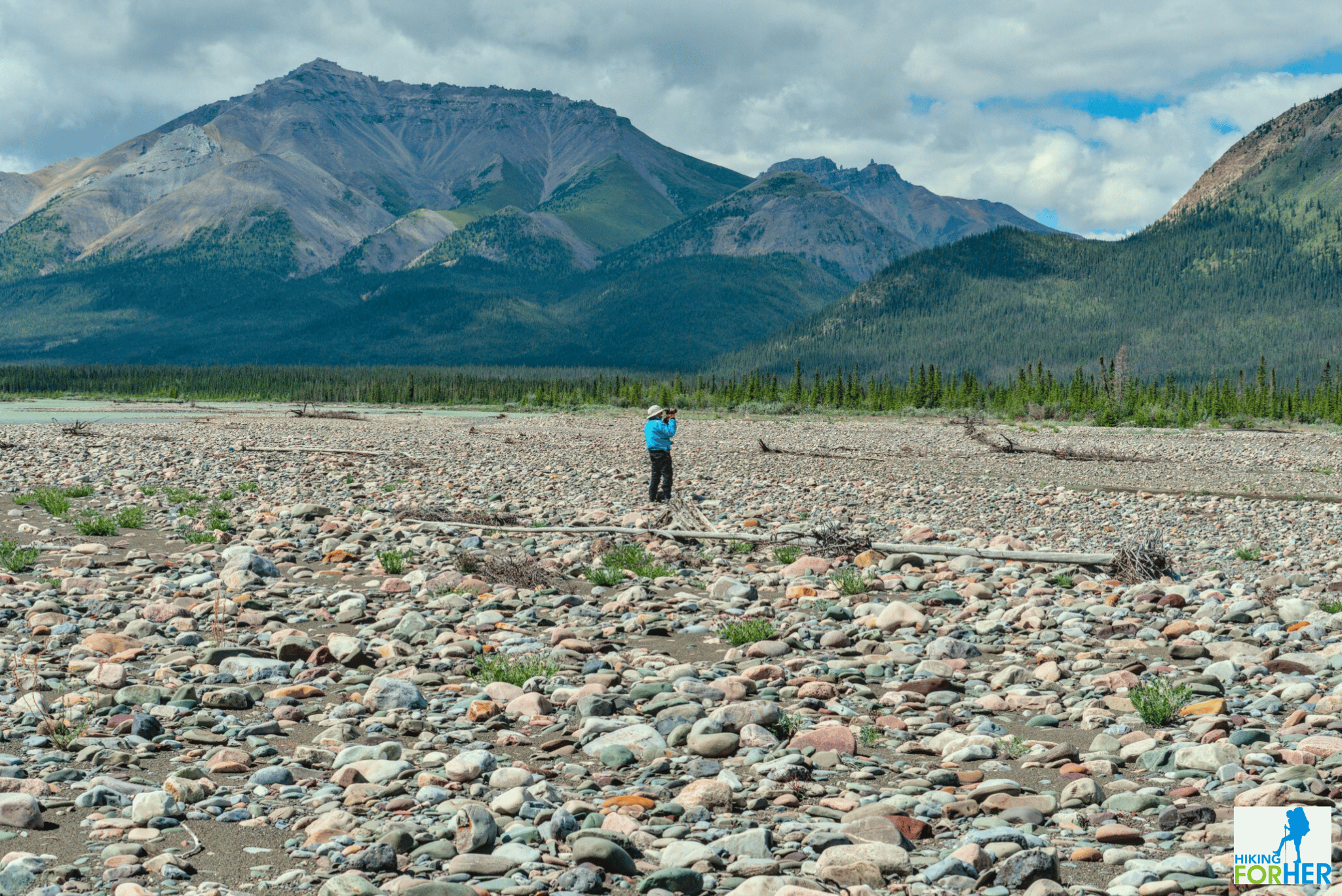 female hiker taking photos on a rocky river bed with unnamed peak in the distance