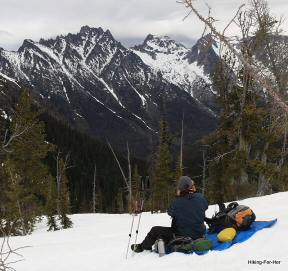 Female hiker sitting on a blue tarp in the snow with a big view of a snow covered mountain