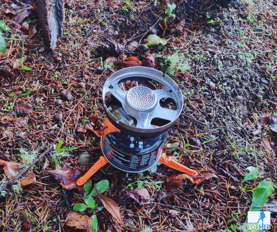 Jetboil MicroMo cooking system black fuel canister sitting on orange plastic stabilizer with burner assemply attached, sitting on ground in Hiking For Her's gear review