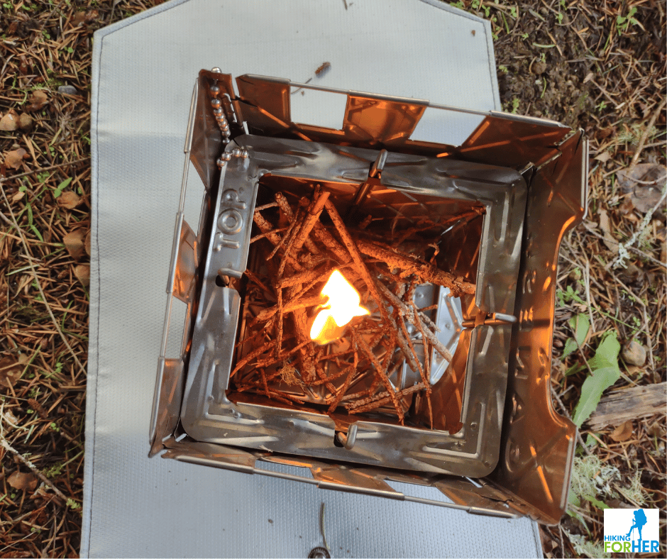 Ganesha ultralight wood burning backpacking stove with twigs and small flame burning in the interior, siting on a fire resistant mat