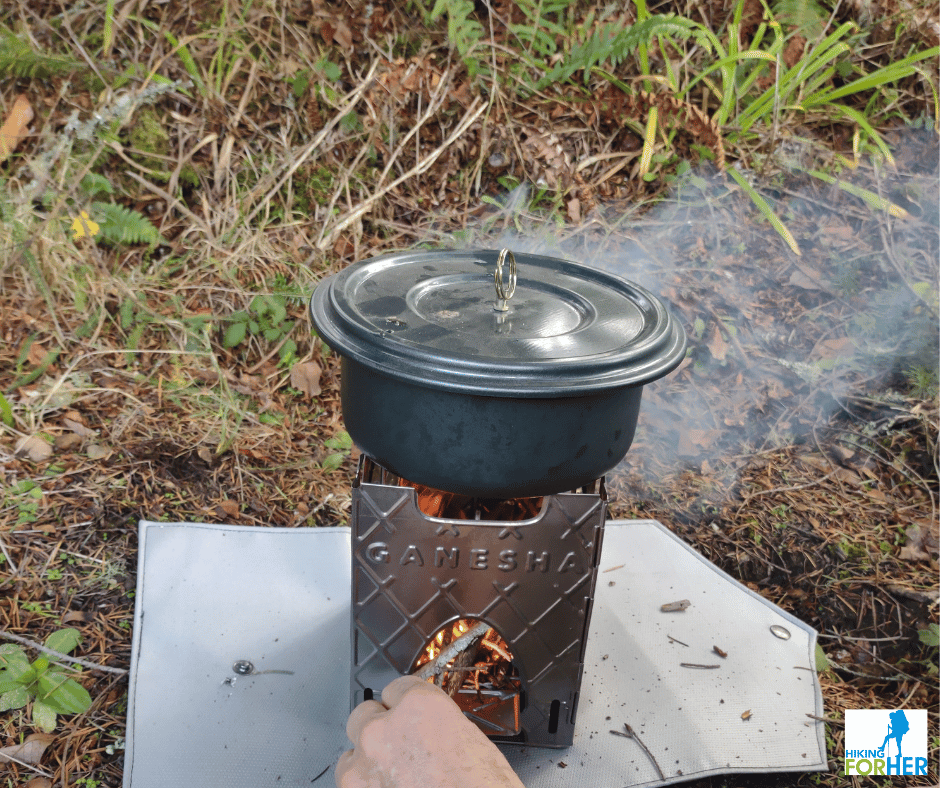 Ganesha backpacking twig stove with flame and a hand feeding small twigs into the fire