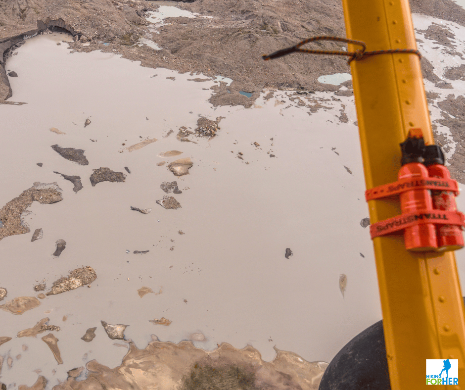Bear spray cans lashed to the strut of a bushplane as it flies over icy ponds on a glacier