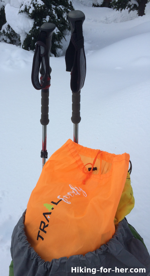 Hiking poles and orange lunch sack on snowy trail