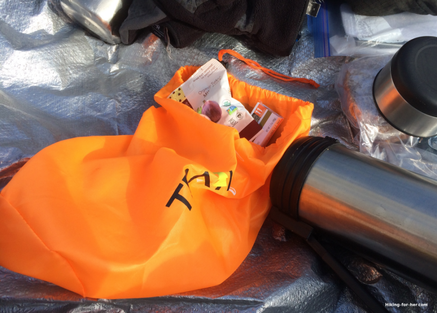 bright orange sack filled with hiking snacks and lunch on a silver reflective tarp with metal thermos nearby