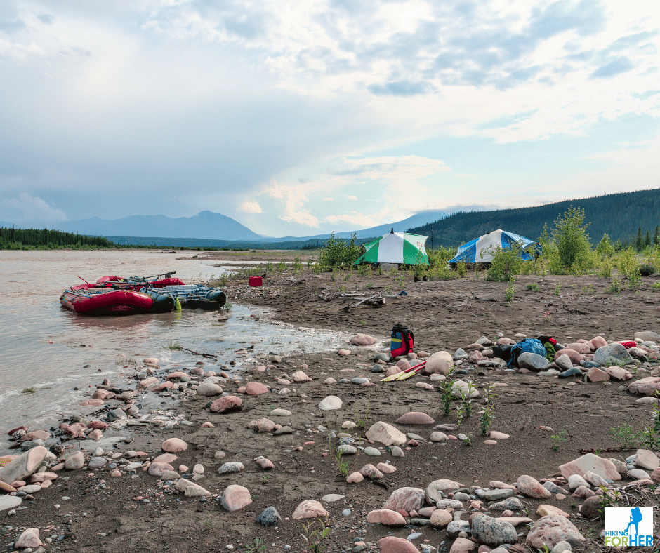 rafts tied up at river's edge with two striped kitchen tents in background and rafting gear strewn on riverbank