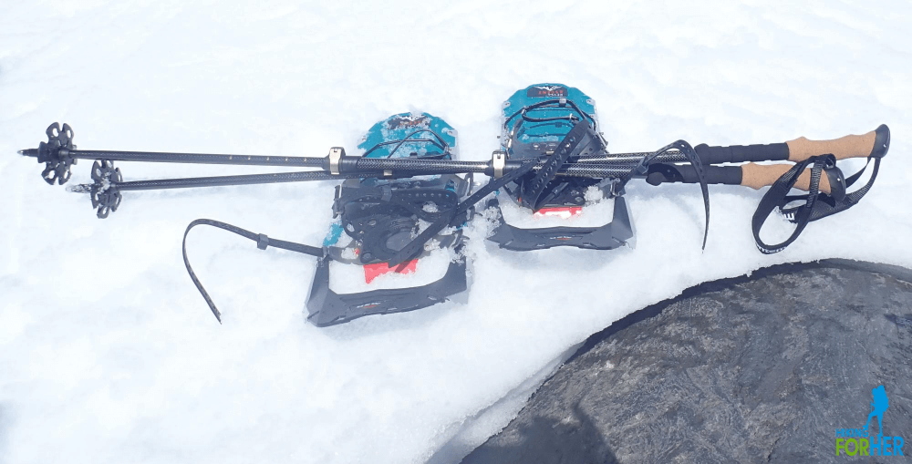 snowshoes and trekking poles sitting on snow near large boulder