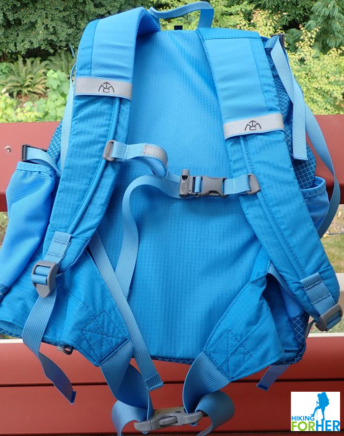 Women's blue hiking day pack from the back, showing shoulder straps, sternum belt, side pockets and haul strap