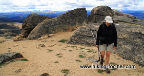 female hiker with trekking poles and backpack on a trail surrounded by large boulders