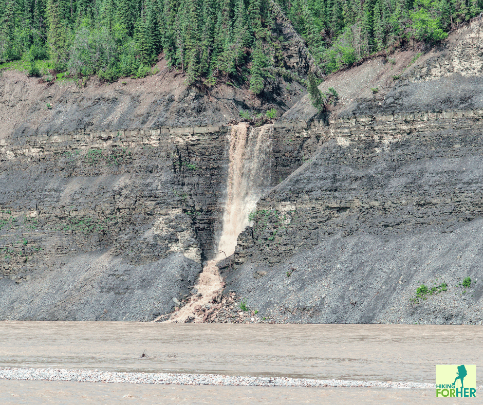 Waterfall cascading out of rocky cliff on a riverbank