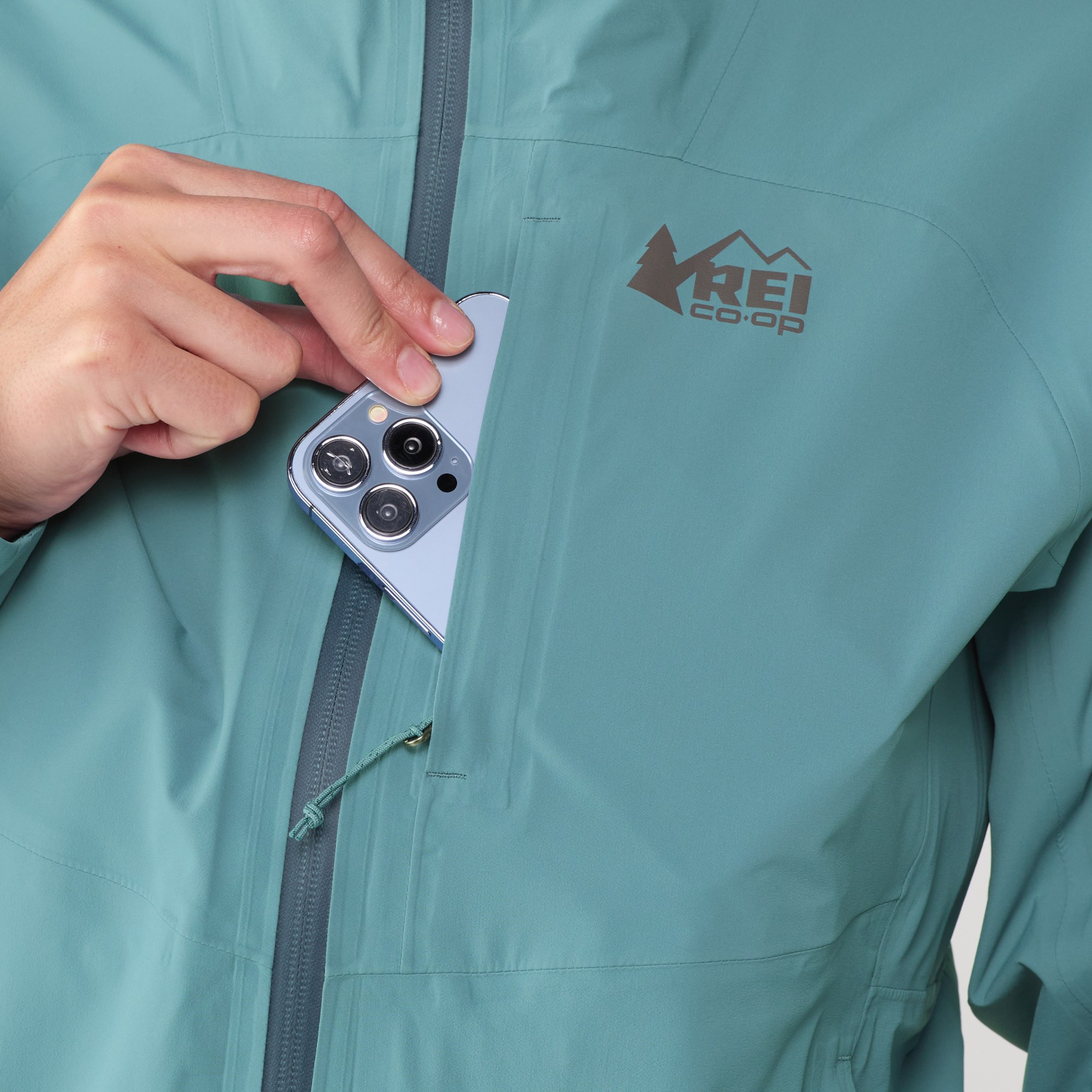 blue REI Xerocloud rain jacket showing cell phone being stored in chest zippered pocket
